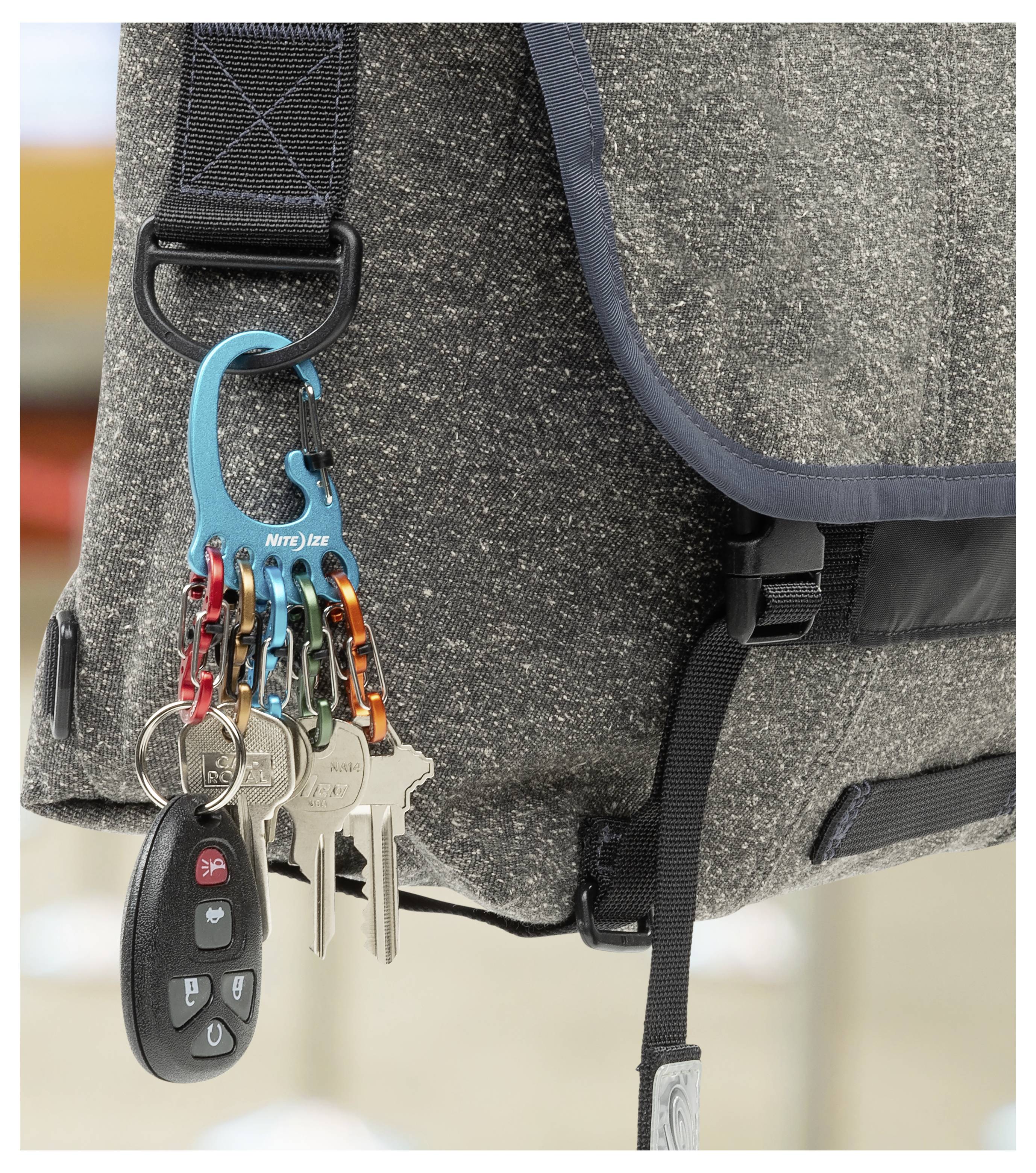 Szara torba materiałowa z niebieskim karabińczykiem przymocowanym do paska, na którym zawieszonych jest kilka kluczy oraz pilot do samochodu.