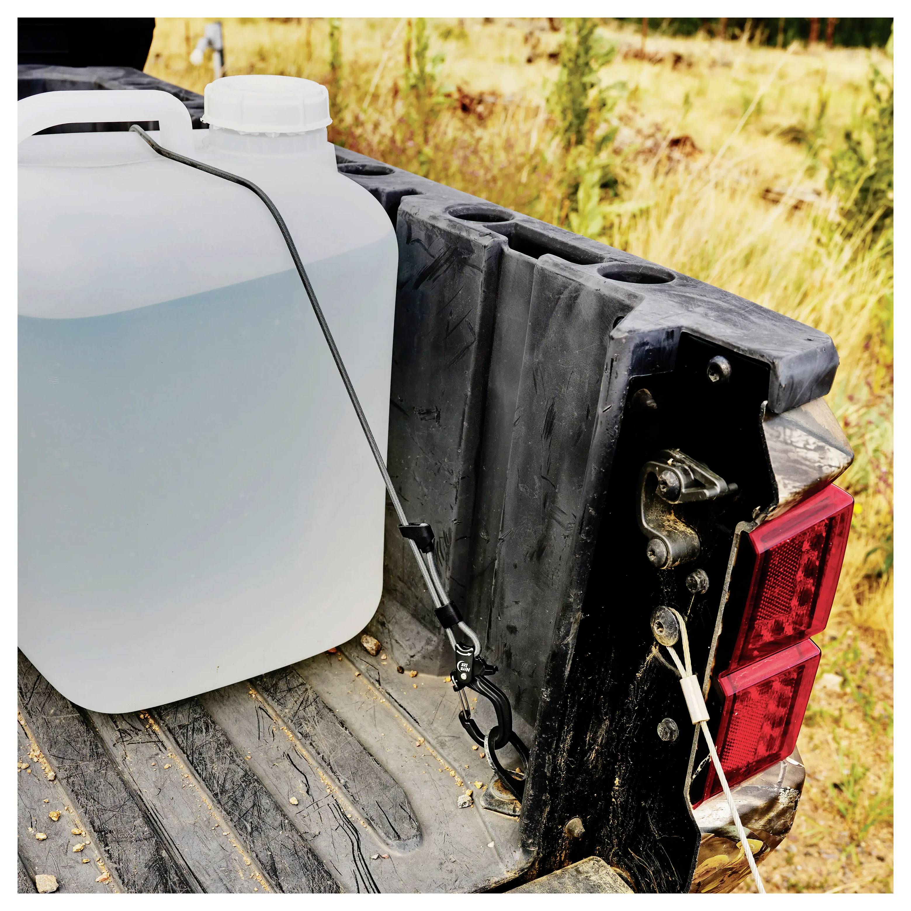 Duży pojemnik na wodę stoi na otwartej tylnej klapie pojazdu. Do kontenera podłączony jest wąż, ciągnący się na bok, gotowy do użycia.