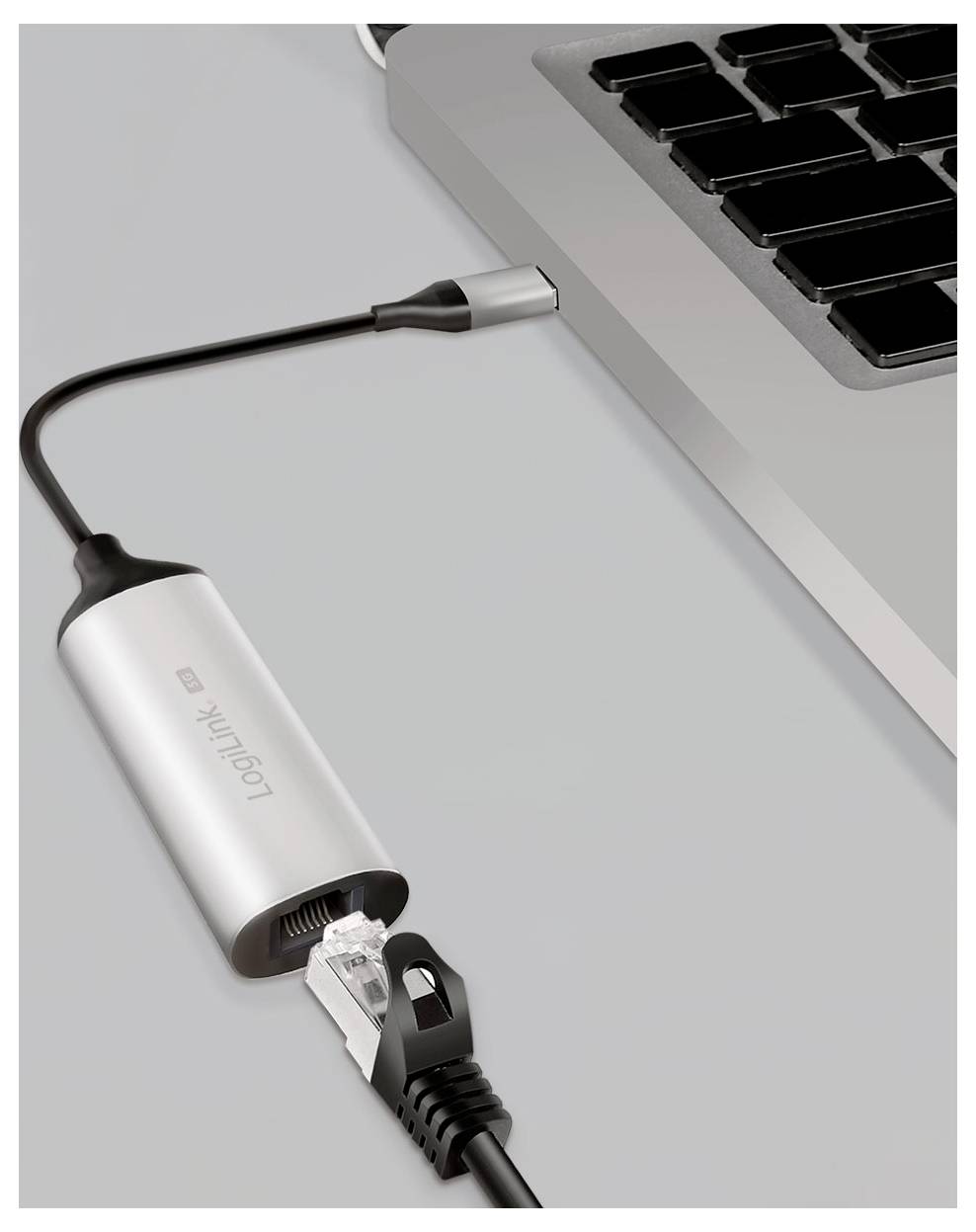Srebrny adapter USB-C do Ethernetu łączy czarny kabel sieciowy z laptopem, umożliwiając komputerowi przewodowy dostęp do internetu.