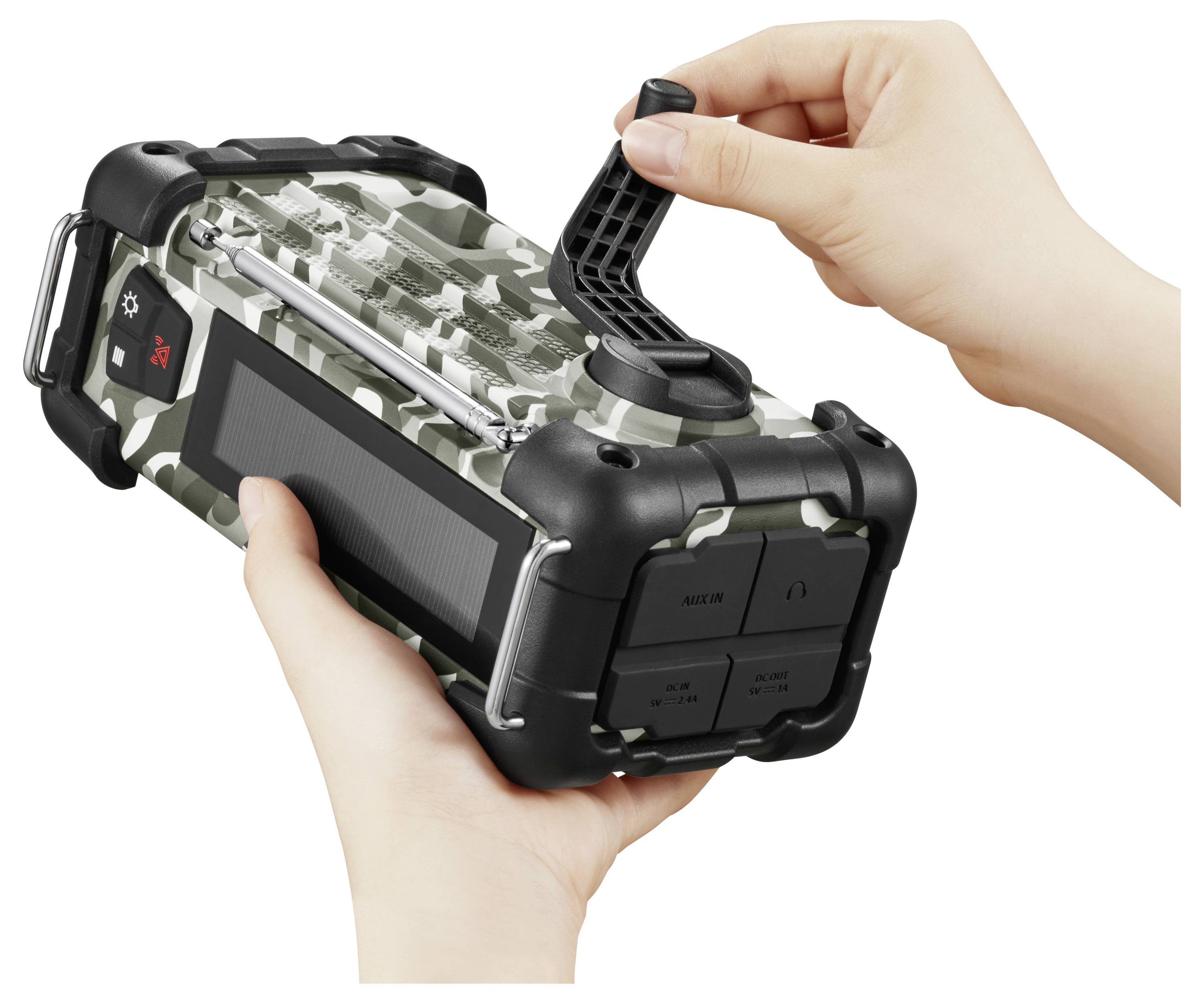 Ręce obsługujące korbę na maskowanym, przenośnym radiu z przyciskami i panelem słonecznym, sugerujące, że jest przeznaczony do użytku na świeżym powietrzu lub w sytuacjach awaryjnych.