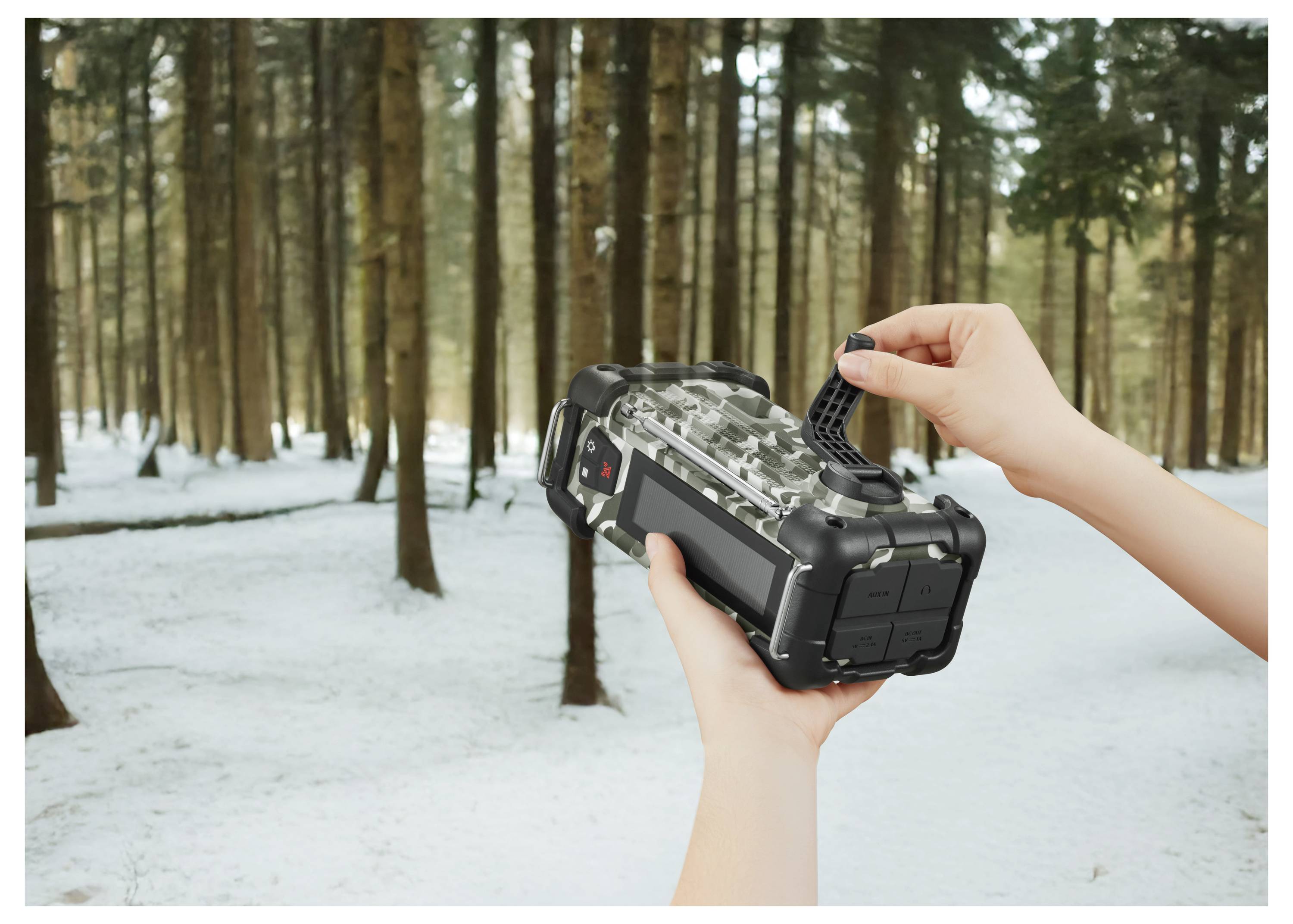 Osoba trzyma czarną kamerę do obserwacji dzikiej przyrody w śnieżnym lesie, dostosowując jej ustawienia. W tle widoczne są wysokie drzewa.