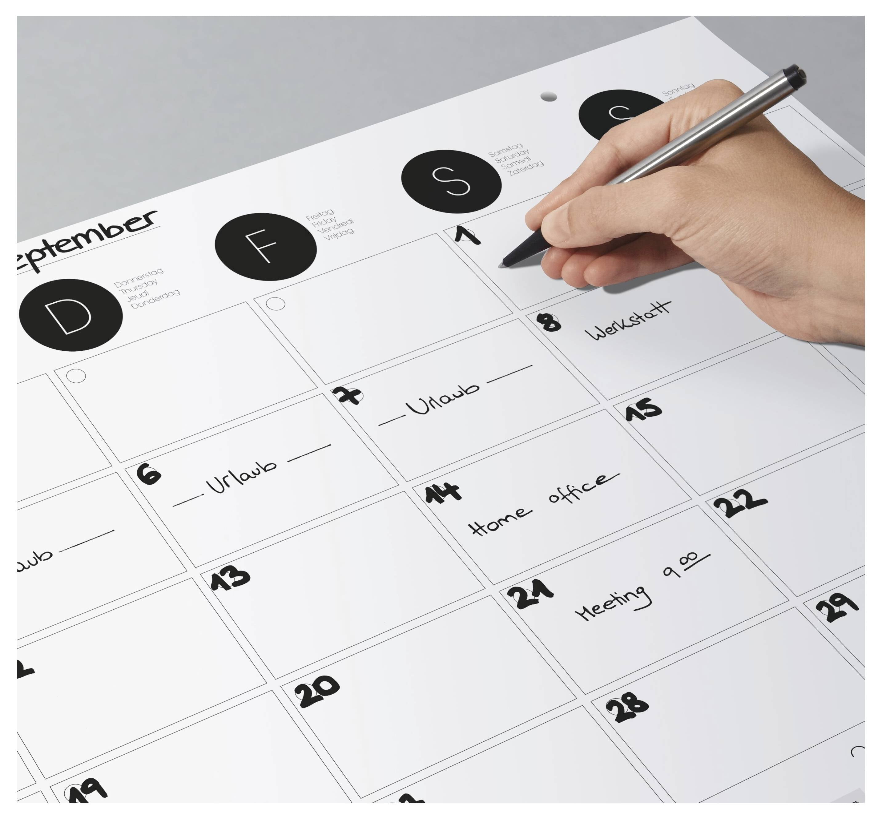 Dłoń trzymająca długopis zaznacza kalendarz wrześniowy wydarzeniami takimi jak 'Urlop', 'Praca zdalna' oraz 'Spotkanie godz. 9.00'.
