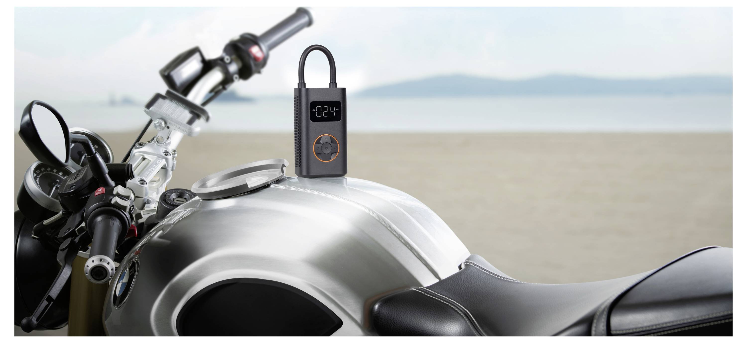Przenośna pompka powietrza z wyświetlaczem cyfrowym stoi na zbiorniku paliwa motocykla na plaży.