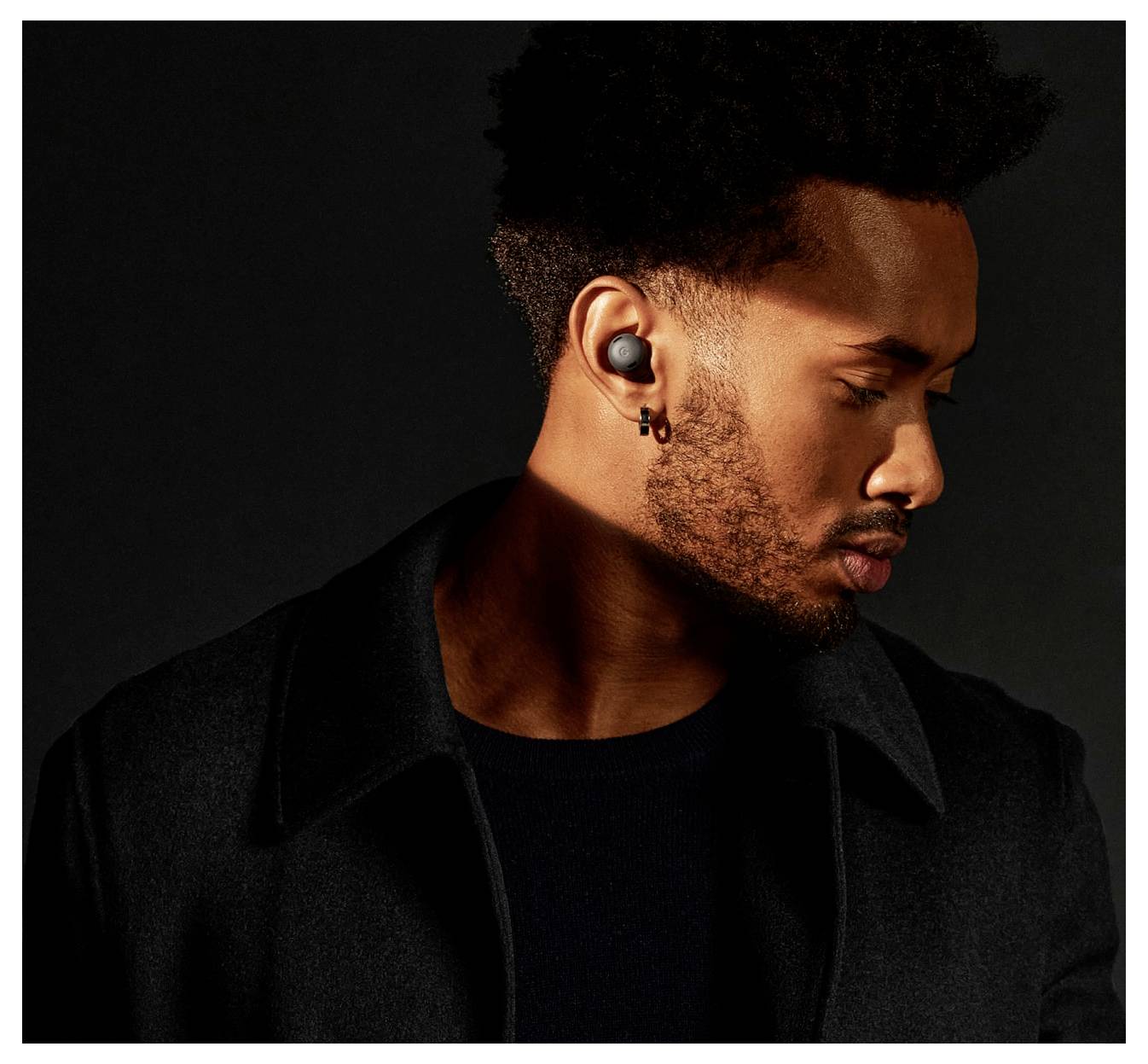 Osoba nosząca słuchawki douszne, spoglądająca w dół, w słabo oświetlonym otoczeniu.