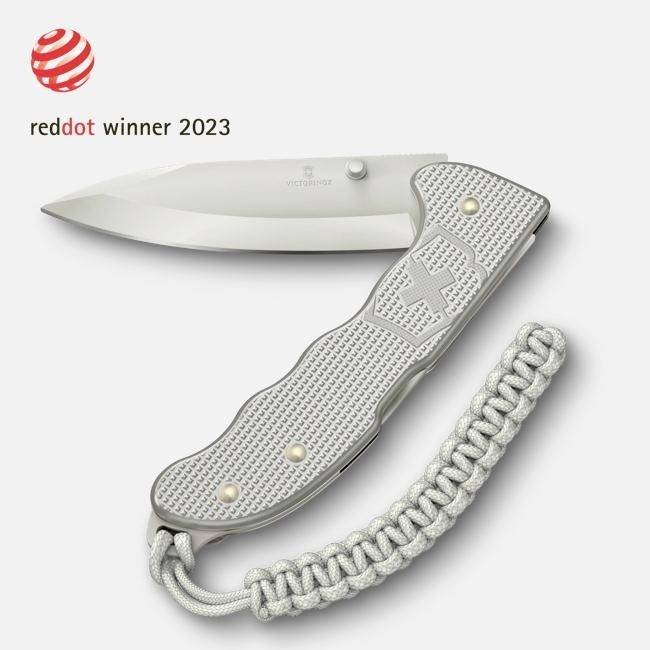 Srebrny nóż składany z fakturowaną rączką i sznurem paracordowym, pokazany z tekstem nagrody „reddot winner 2023".