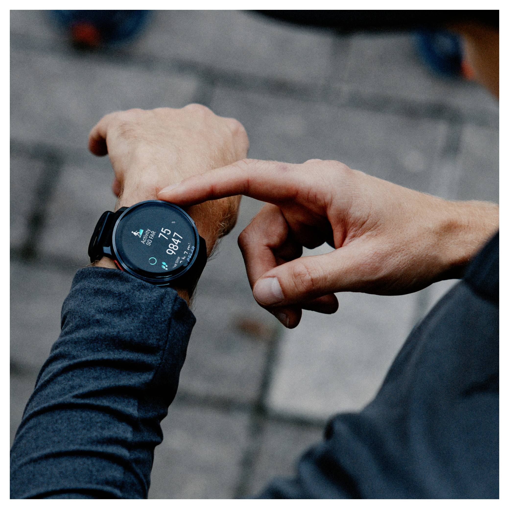 Osoba w ciemnym rękawie sprawdza smartwatch wyświetlający godzinę '8:47' na rozmytym tle kamiennego bruku.