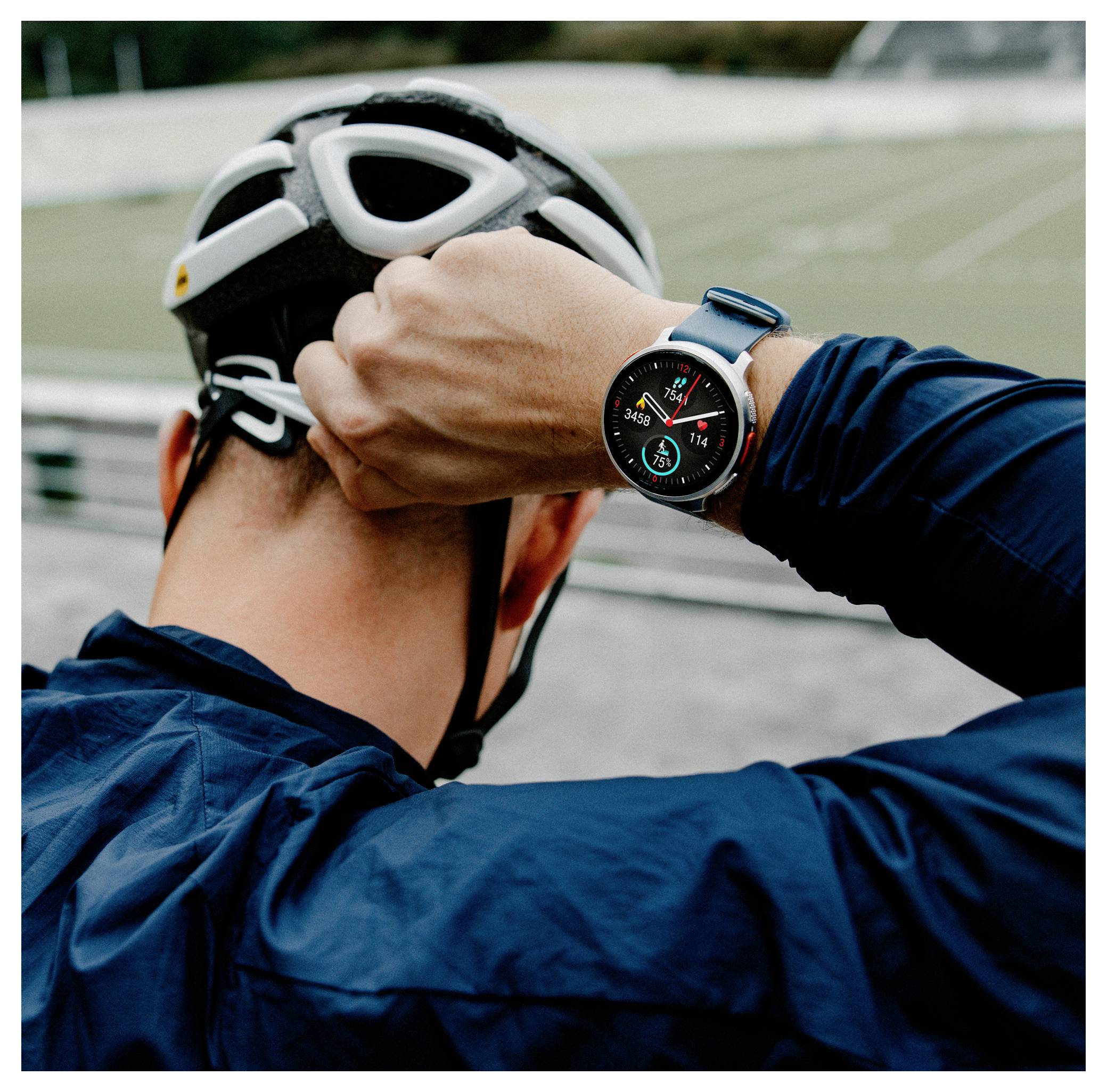 Rowerzysta reguluje pasek kasku, mając na nadgarstku smartwatch wyświetlający szczegóły śledzenia aktywności fizycznej, stojąc w pobliżu boiska sportowego na świeżym powietrzu.