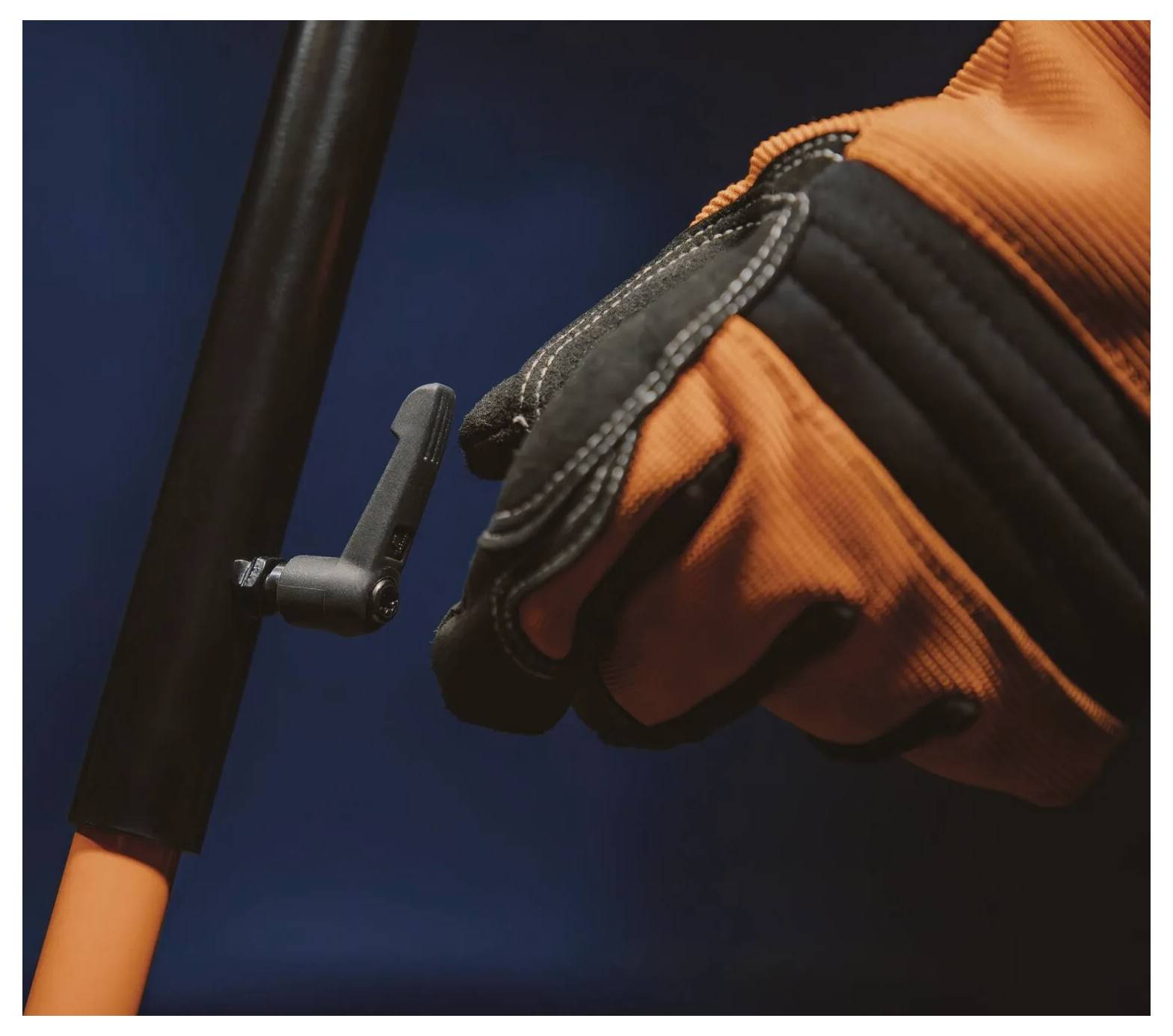 Ręka w rękawiczce ściska dźwignię na drążku na ciemnym tle, wskazując na kontrolę lub obsługę narzędzia lub sprzętu.