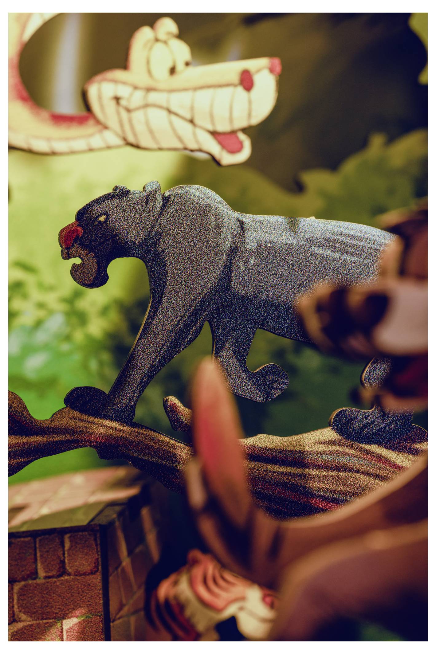 Figurka komiksowej pantery o otwartych ustach stoi na gałęzi w scenerii dżungli, za nią znajduje się czerwona figura węża.