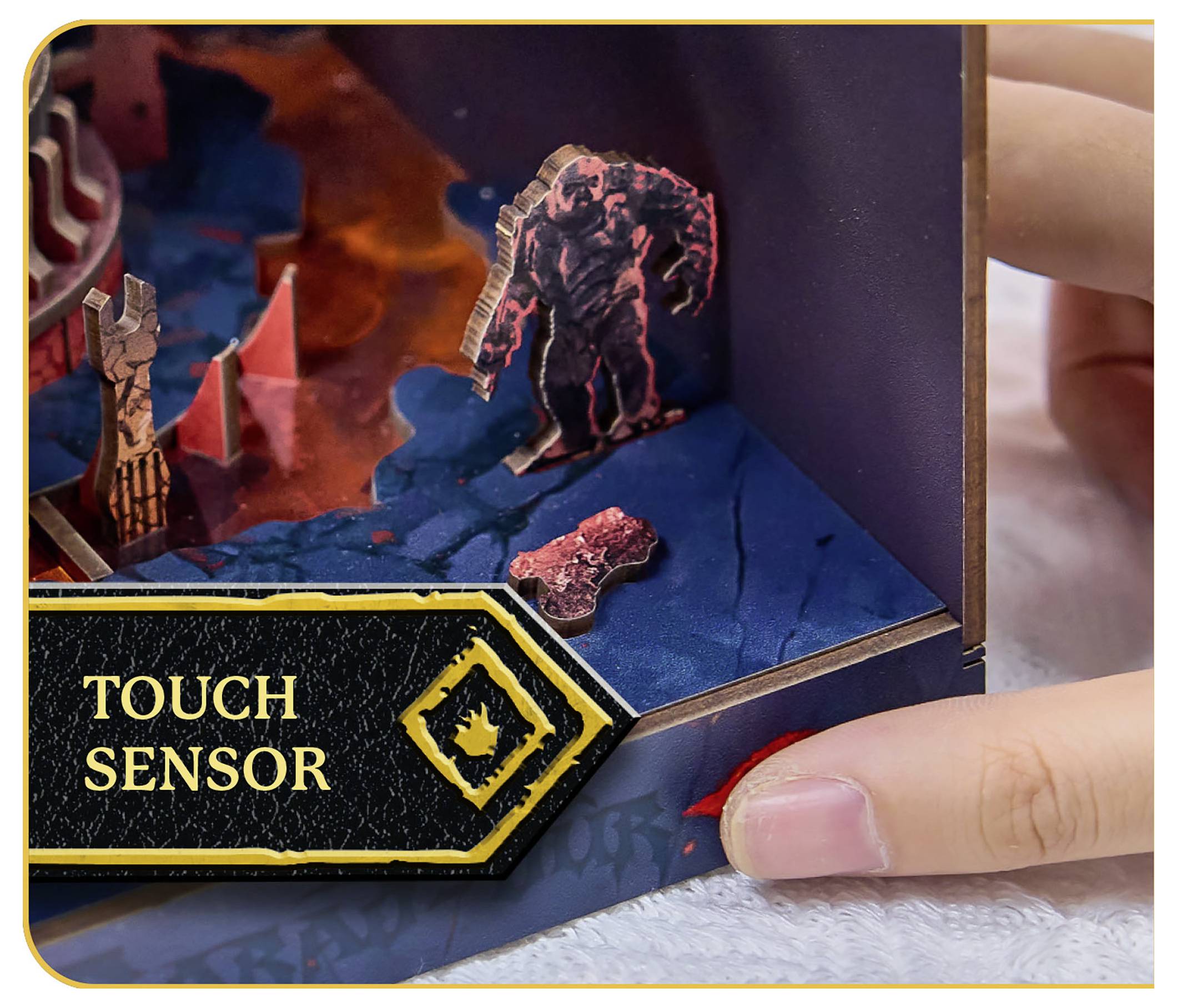 Osoba wchodzi w interakcję z grą planszową, aktywując obszar 'CZUJNIKA DOTYKOWEGO', który uwalnia figurkę na kolorową, fakturalną powierzchnię.