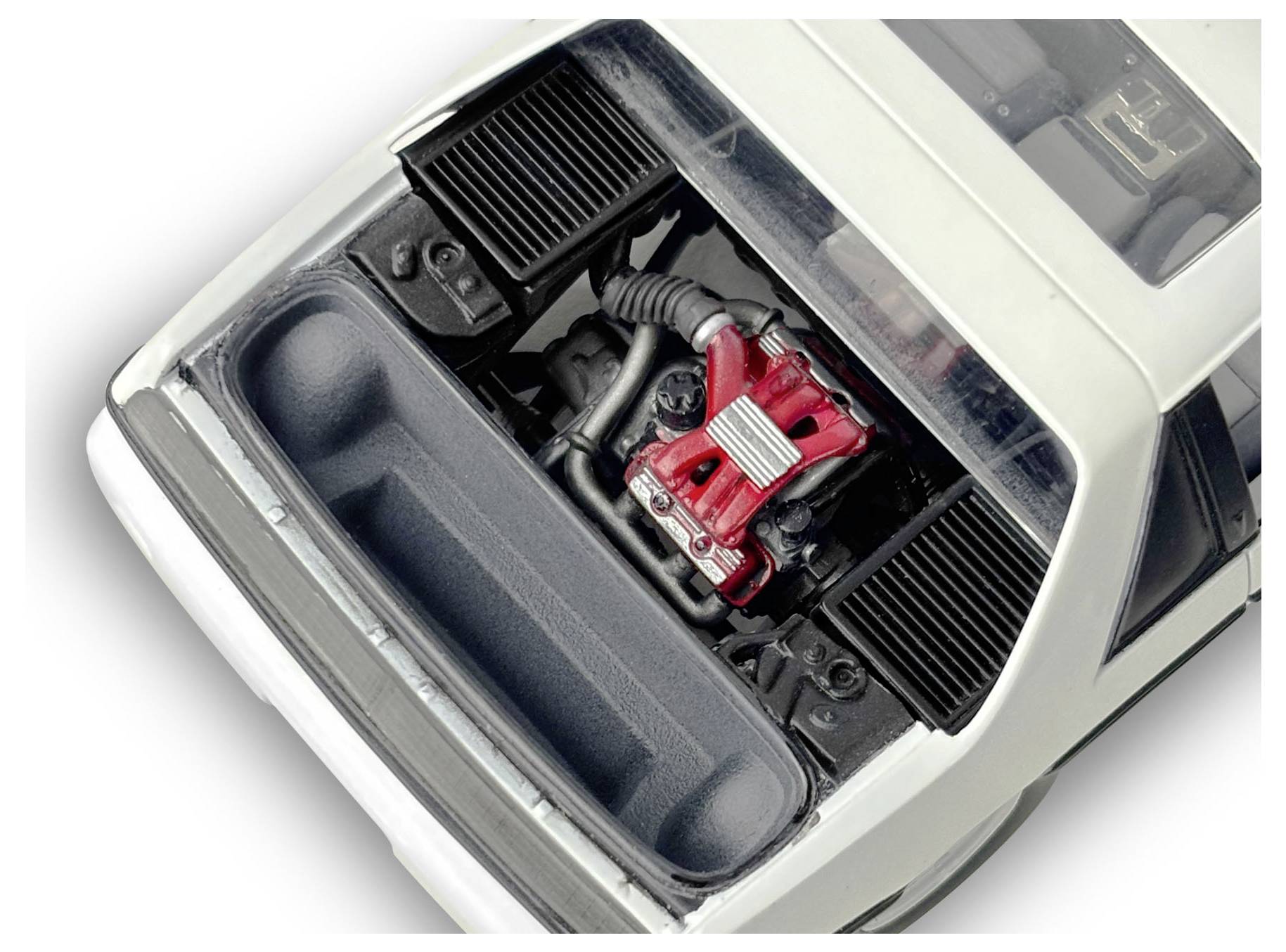 Model samochodu z otwartą komorą silnika, ukazujący szczegółowe komponenty silnika w kolorach czerwonym i srebrnym wewnątrz białego samochodu.