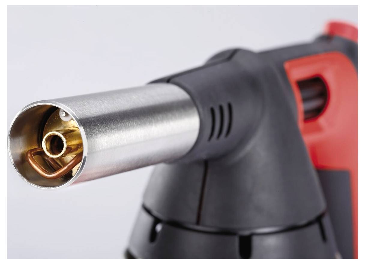 Zbliżenie palnika gazowego z metalową dyszą, wyposażonego w pomarańczowo-czarną rączkę, ze szczególnym naciskiem na strefę zapłonu.