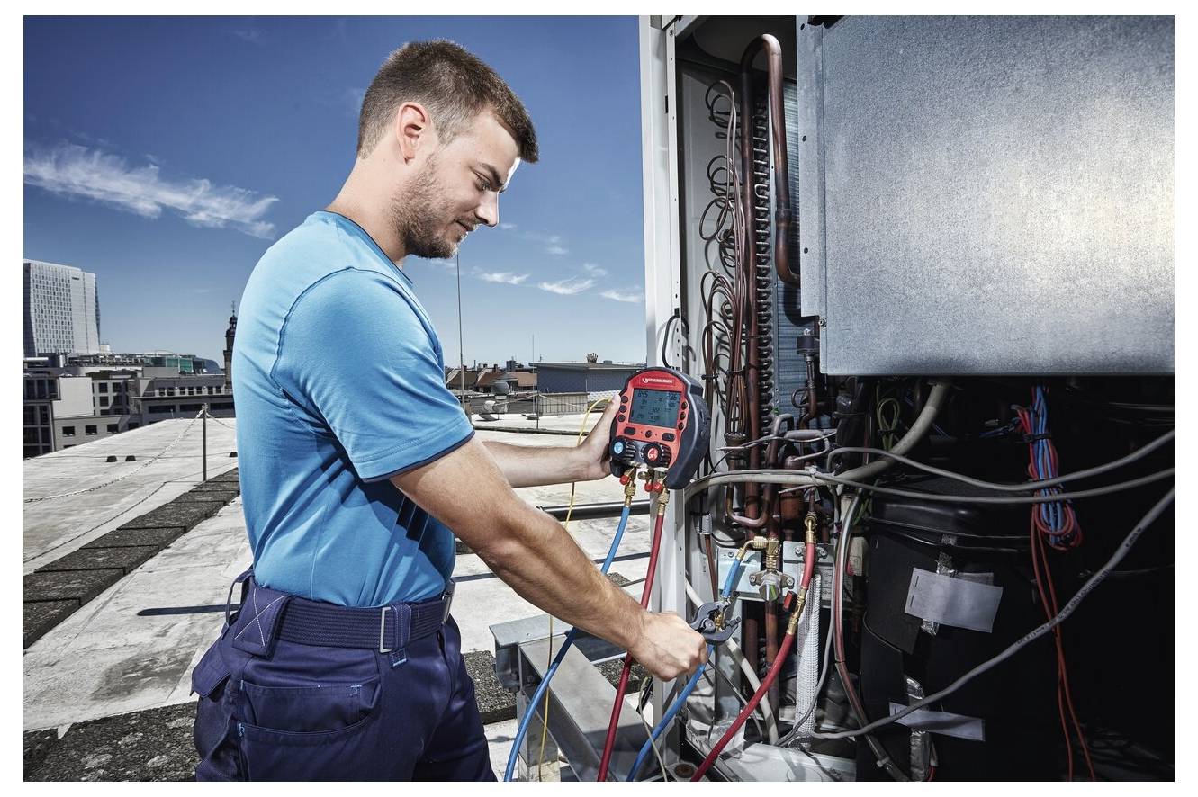 Technik na dachu używa sprzętu diagnostycznego do kontroli systemu HVAC, sprawdzając poziomy ciśnienia oraz połączenia instalacji w słoneczny dzień.