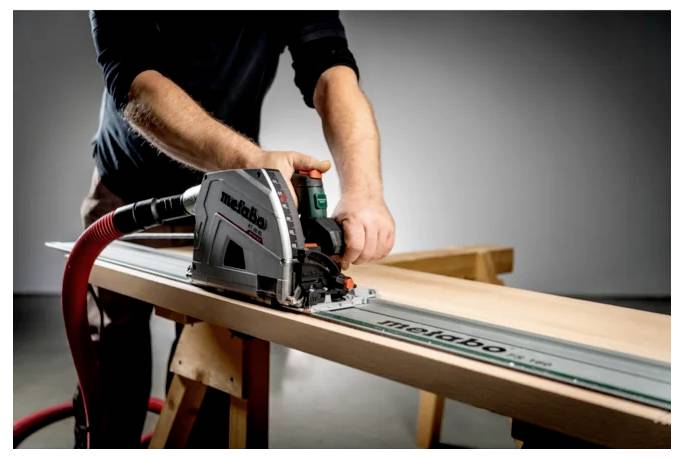 Osoba używająca przenośnej piły tarczowej z prowadnicą do cięcia długiej drewnianej deski w warsztacie.