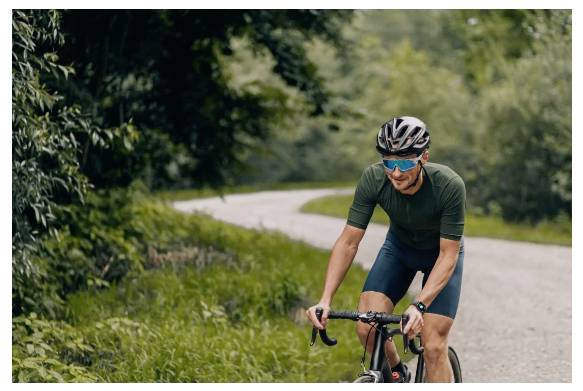 Osoba jedzie na rowerze krętą ścieżką przez gęsty, zielony las, ubrana w kask, okulary przeciwsłoneczne i strój rowerowy, wyglądająca na skoncentrowaną.
