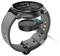 Smartwatch na stacji dokującej, której podstawa znajduje się pod tarczą zegarka. Na ekranie wyświetlane są liczne tarcze zegarowe i ikony.