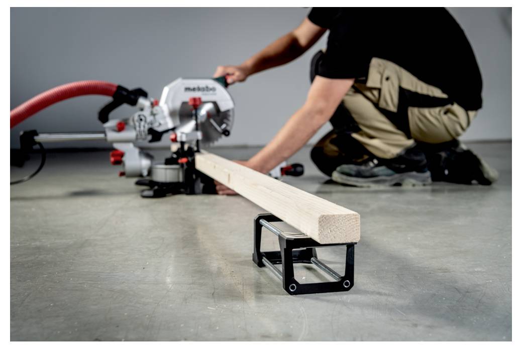 Osoba używająca piły stołowej do cięcia drewnianej belki w warsztacie. Nacisk położony jest na precyzyjne wyrównanie drewna z ostrzem piły.