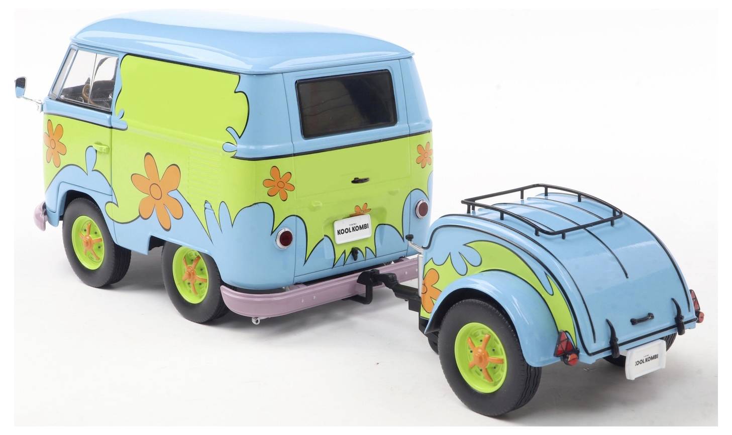 Jasno zabarwiony niebieski i zielony van z pomarańczowymi wzorami kwiatowymi holuje dopasowaną małą przyczepę, oba elementy posiadające żywe wzornictwo.