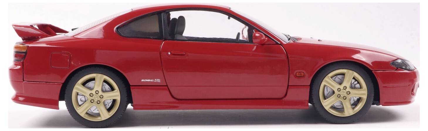 Widok z boku czerwonego samochodu sportowego coupe z złotymi felgami aluminiowymi, z dużym tylnym skrzydłem i przyciemnianymi oknami. Samochód znajduje się na białym tle.