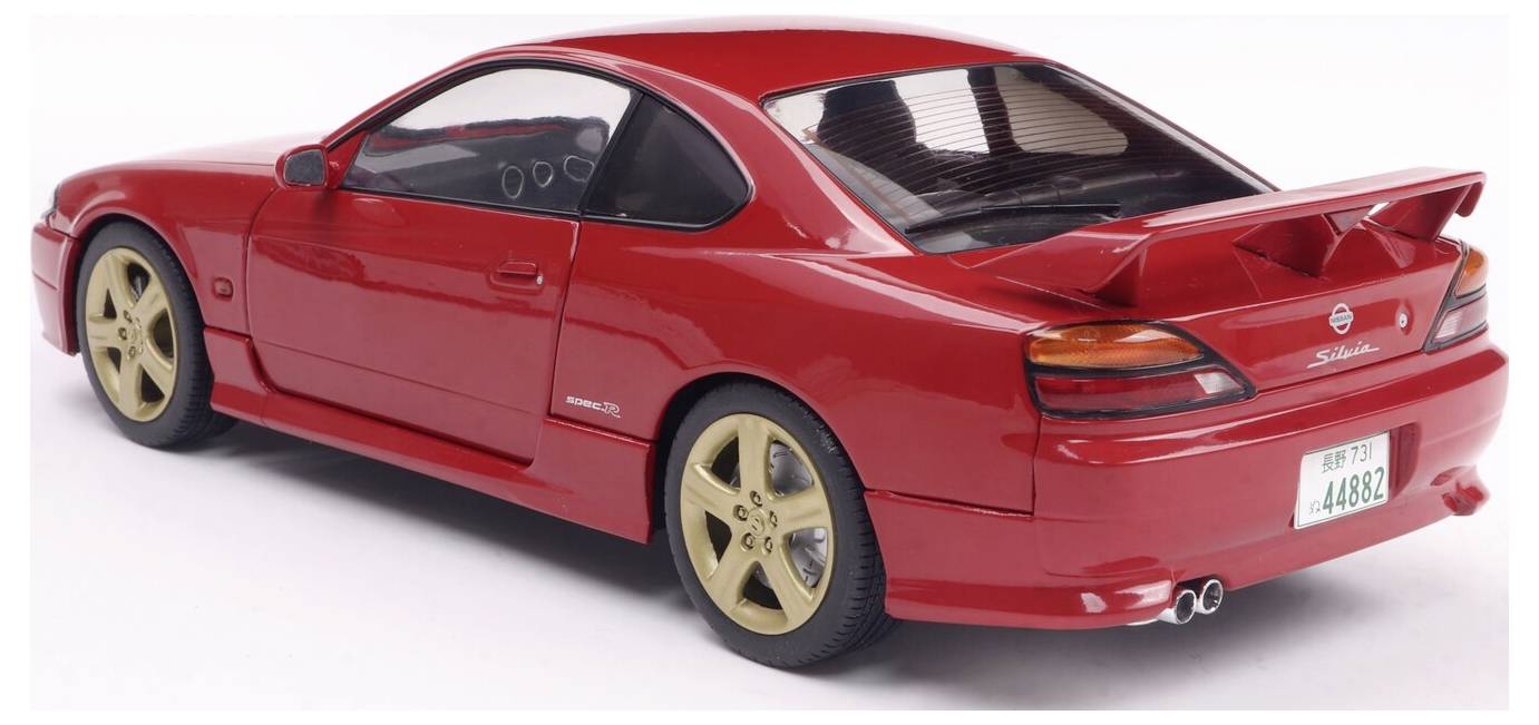 Czerwony samochód sportowy z tylnym spojlerem i złotymi felgami, sfotografowany z tylnego boku. Samochód jest kompaktowym modelem coupe.