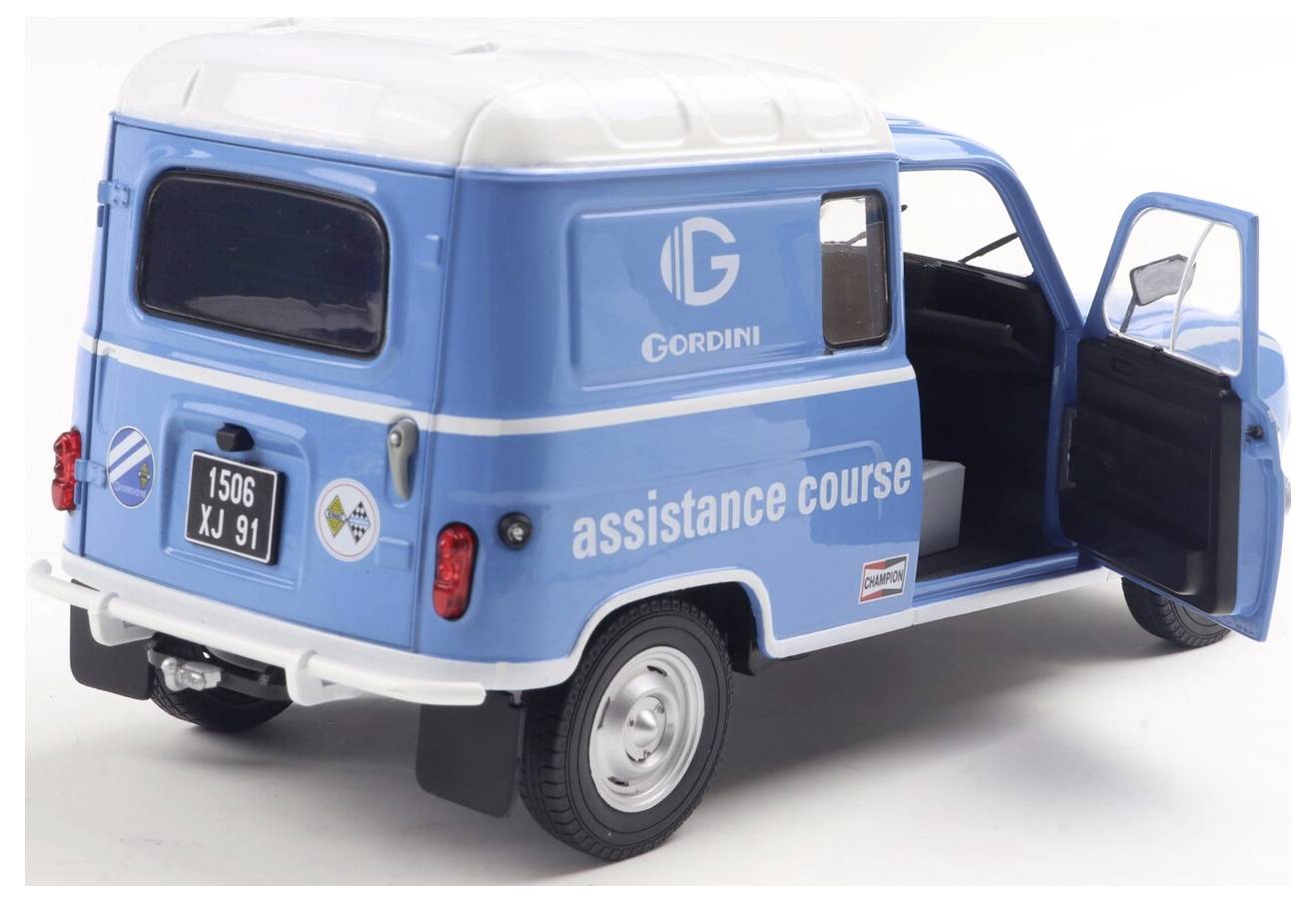 Niebieski zabytkowy van z logo 'Gordini' i napisem 'assistance course' na boku. Tylne drzwi są otwarte, ukazując wnętrze.