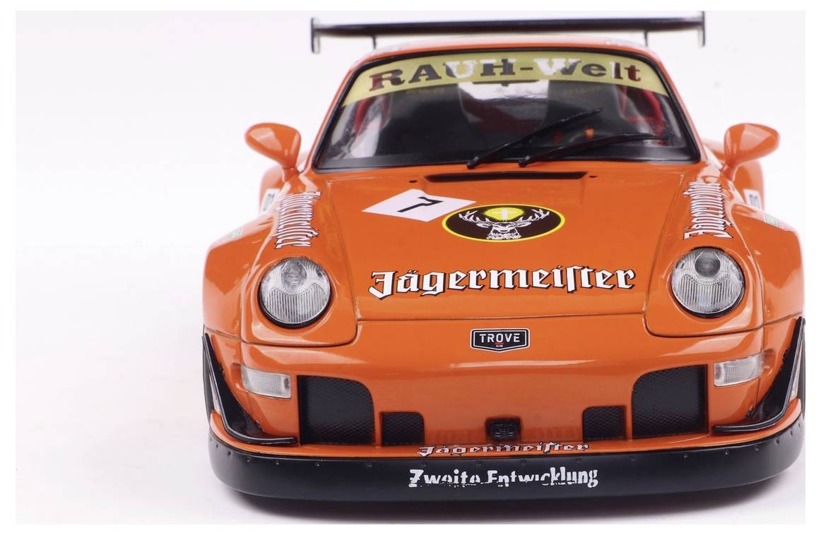 Jasnopomarańczowy samochód sportowy ustawiony przodem, z logo takimi jak 'Jagermeister' i 'RAUH-Welt', z numerem wyścigowym na przedniej szybie.
