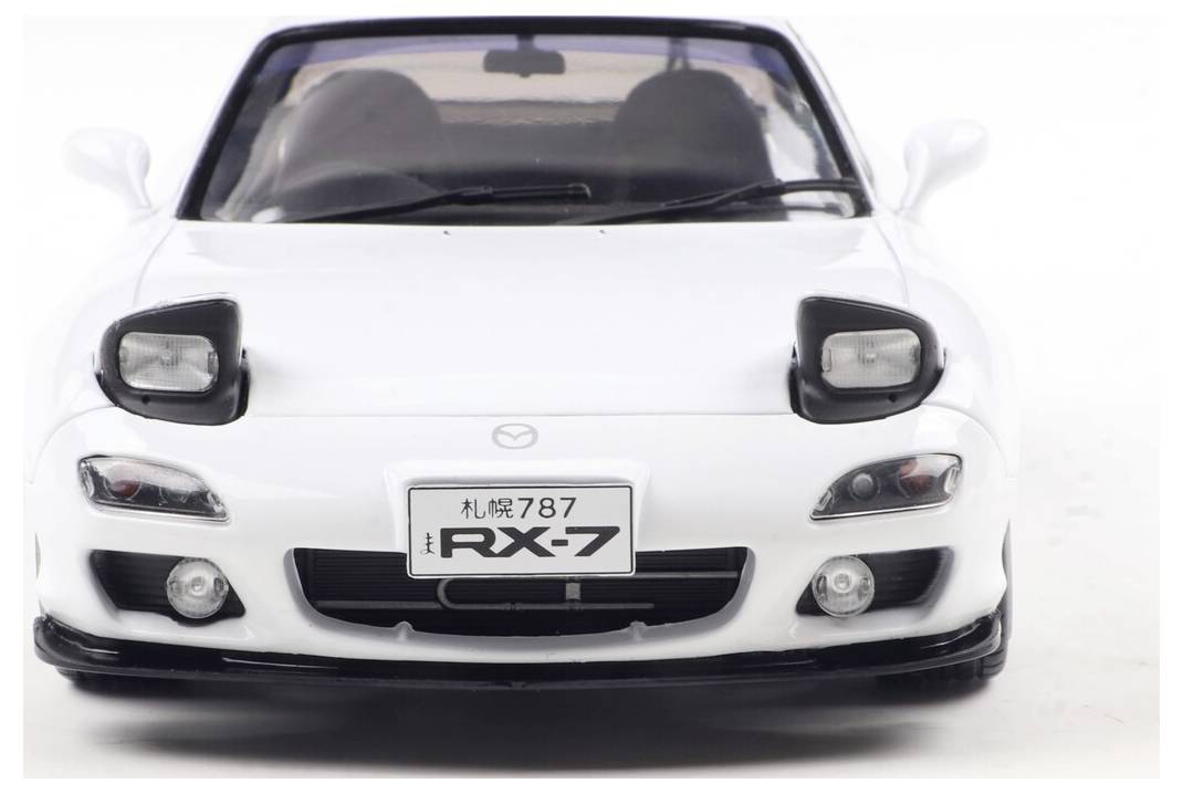 Biały samochód sportowy, widok z przodu, z tablicą rejestracyjną 'RX-7', z wysuwanym reflektorami, stylistyką dwudrzwiową i składanym dachem.