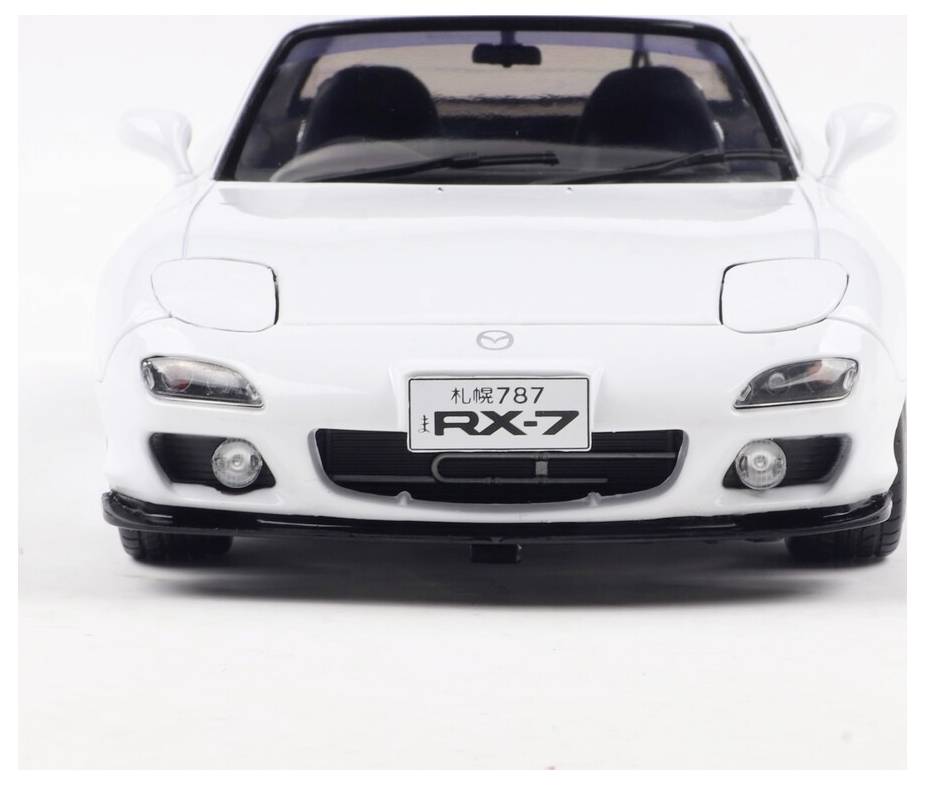 Widok z przodu białego samochodu sportowego z tablicą rejestracyjną 'RX-7'. Samochód ma smukłą sylwetkę z charakterystycznymi reflektorami.