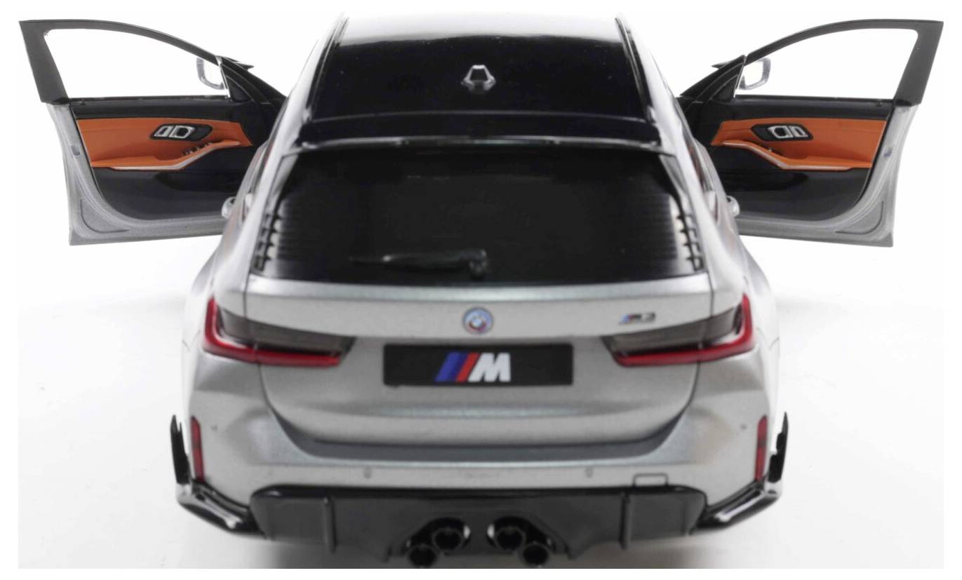 Srebrny samochód z otwartymi tylnymi drzwiami, prezentujący czarno-pomarańczowe wnętrze. Z tyłu pojazdu widoczne logo w kształcie litery 'M'.