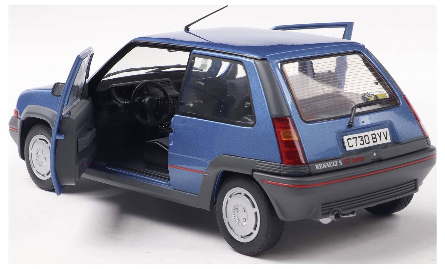 Niebieski model samochodu Renault 5 GT Turbo widziany pod kątem tylno-lewym z otwartymi drzwiami kierowcy, prezentujący wnętrze pojazdu.