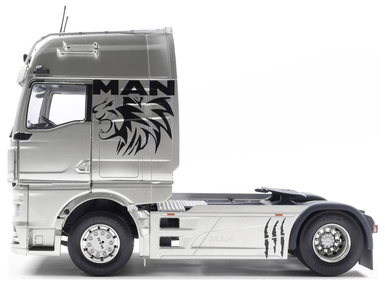 Srebrna ciężarówka widziana z boku z logo "MAN" oraz stylizowanym wzorem lwa na kabinie, prezentująca nowoczesny, opływowy design, bez podłączonej przyczepy.