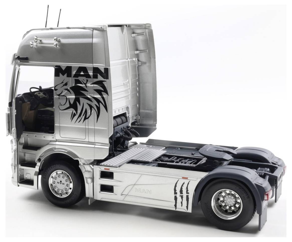 Srebrna kabina samochodu ciężarowego MAN z logo firmy i grafiką lwa, widziana pod kątem tylnym, bez podłączonej przyczepy.