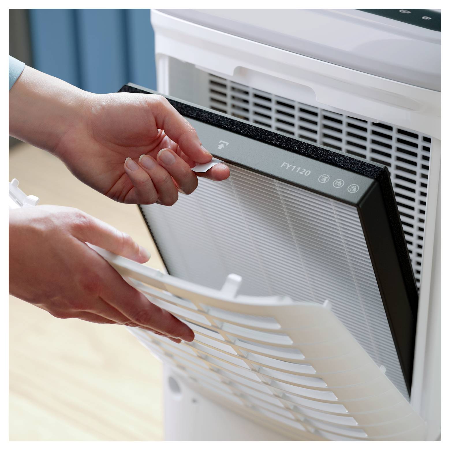 Osoba wymieniająca filtr oczyszczacza powietrza poprzez zdjęcie panelu, odsłaniająca filtr oznaczony napisem 'FY1120', podkreślająca czynności konserwacyjne.