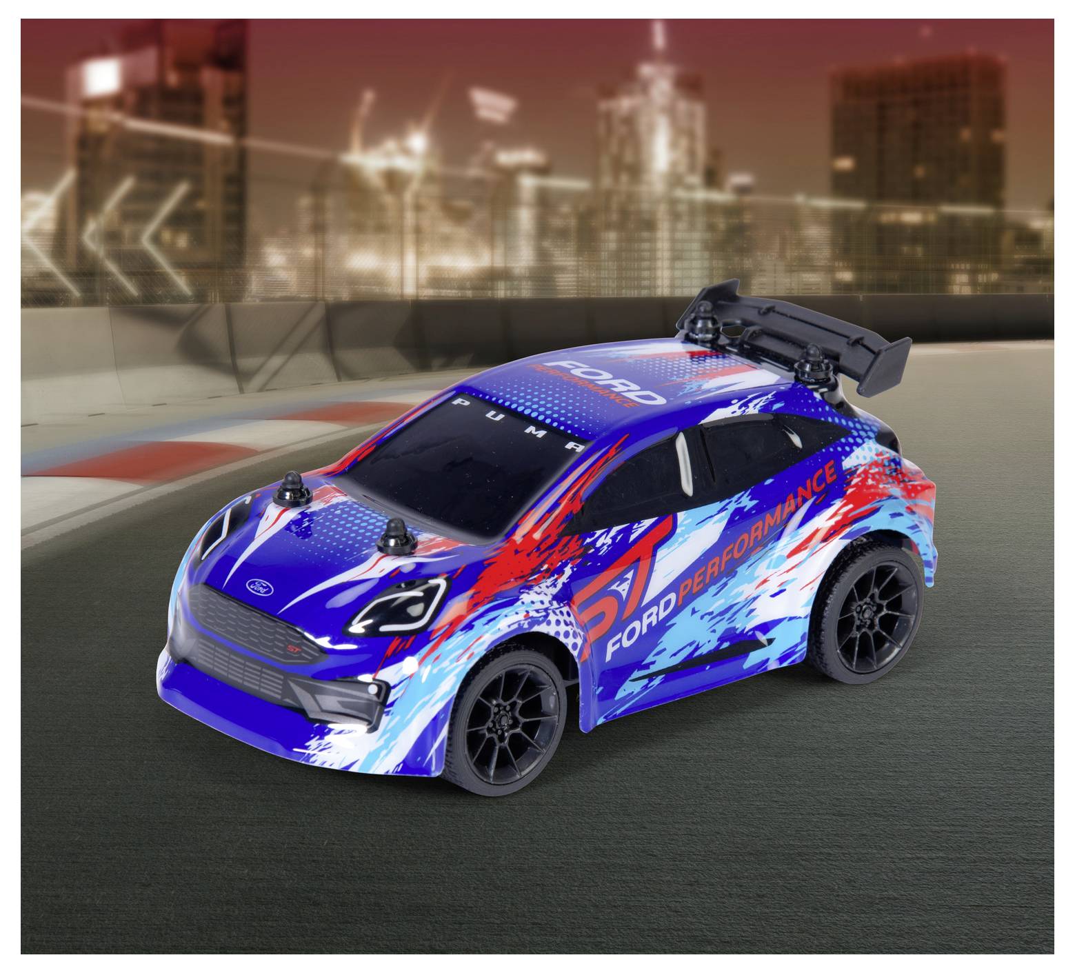 Zabawkowy samochodzik w kolorach niebieskim, czerwonym i białym z oznaczeniem 'Ford Performance' stoi na torze wyścigowym, a w tle widać rozmyty krajobraz miasta.