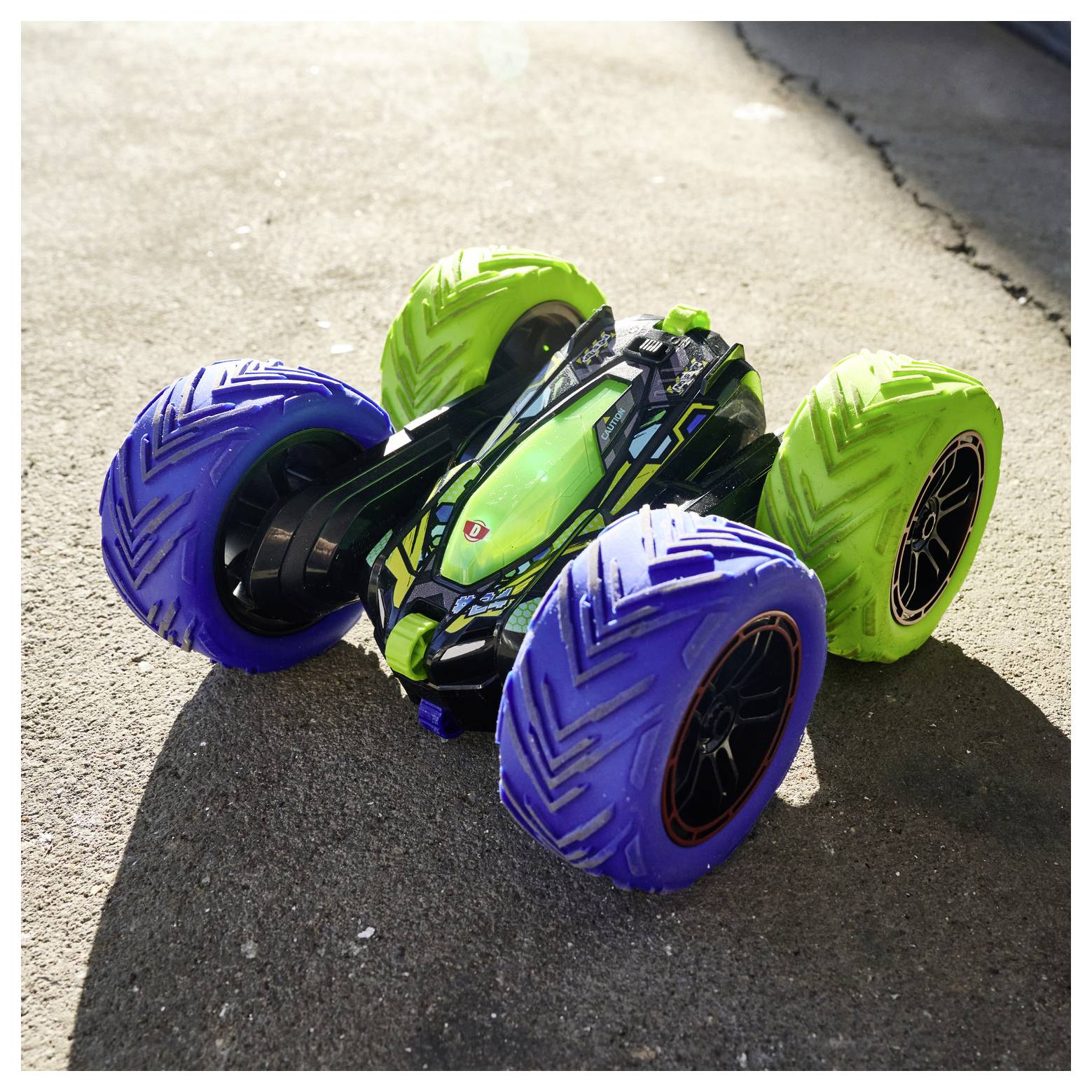 Zielono-czarny samochód zdalnie sterowany z dużymi, kolorowymi oponami jest zaparkowany na betonowej powierzchni, rzucając cień.