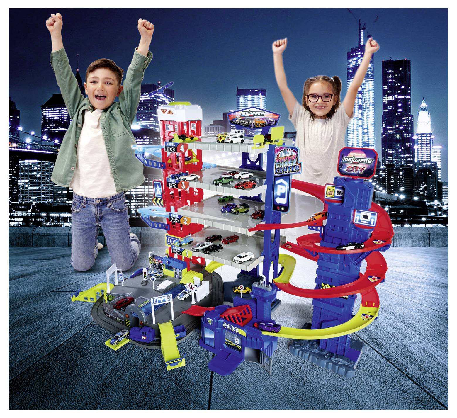 Dwoje dzieci podekscytowanych unosi ręce obok dużego, wielopoziomowego parkingu dla zabawkowych samochodów, z autkami i zjazdami, na tle panoramy miasta.