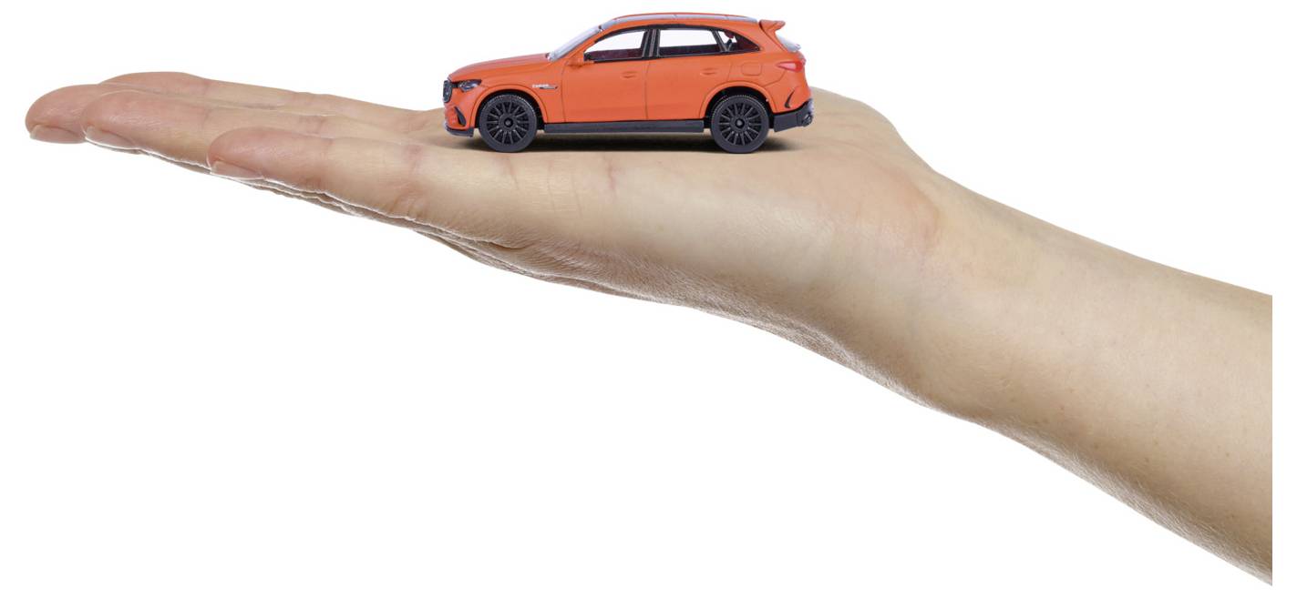 Miniaturowa czerwona zabawka SUV spoczywa na wyciągniętej ludzkiej dłoni na białym tle, podkreślając małą skalę pojazdu.