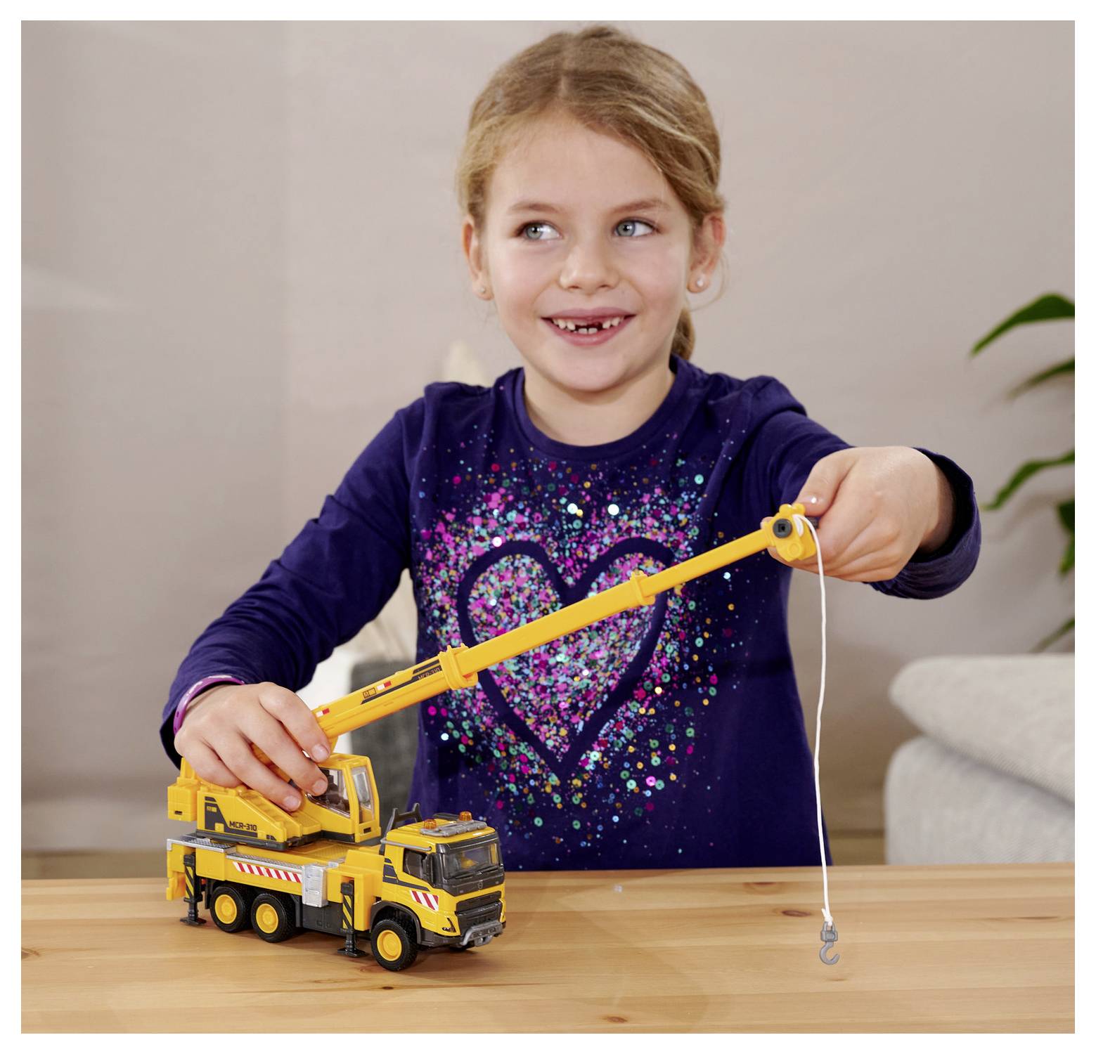 Małe dziecko uśmiecha się, bawiąc żółtą zabawkową dźwigową ciężarówką, wysuwając jej ramię.