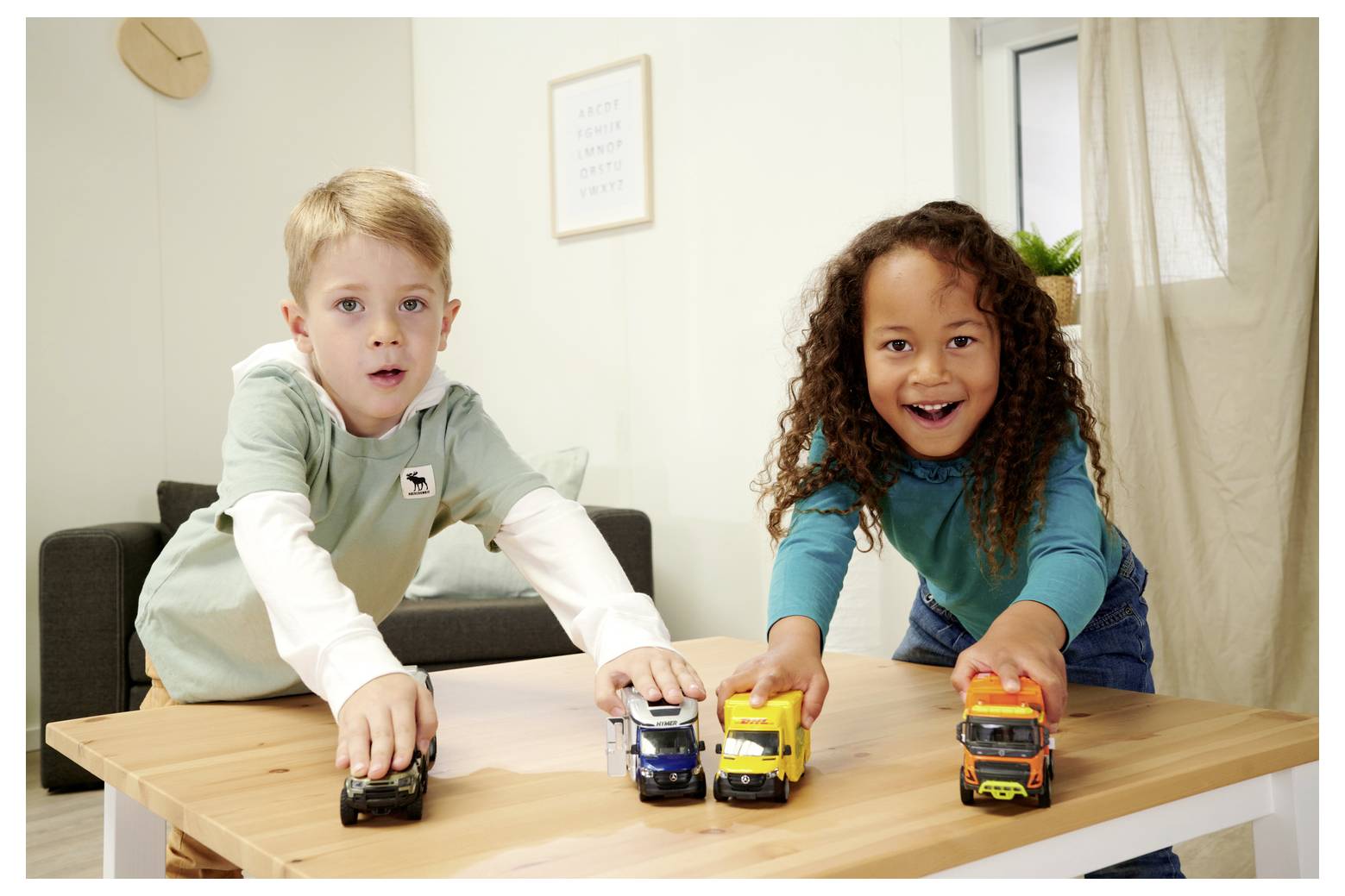 Chłopiec i dziewczynka bawią się samochodzikami zabawkowymi na drewnianym stole w salonie, prezentując radosne miny i różnorodną zabawę.