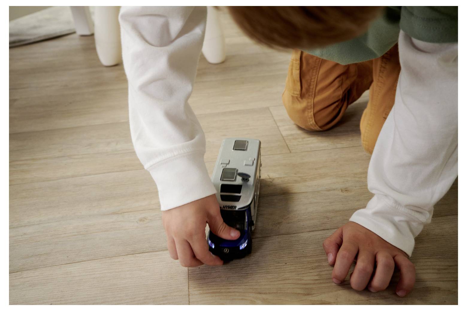 Dziecko bawi się na drewnianej podłodze małym pojazdem zabawkowym, skupiając się z całkowitym zaangażowaniem na jego ustawieniu.