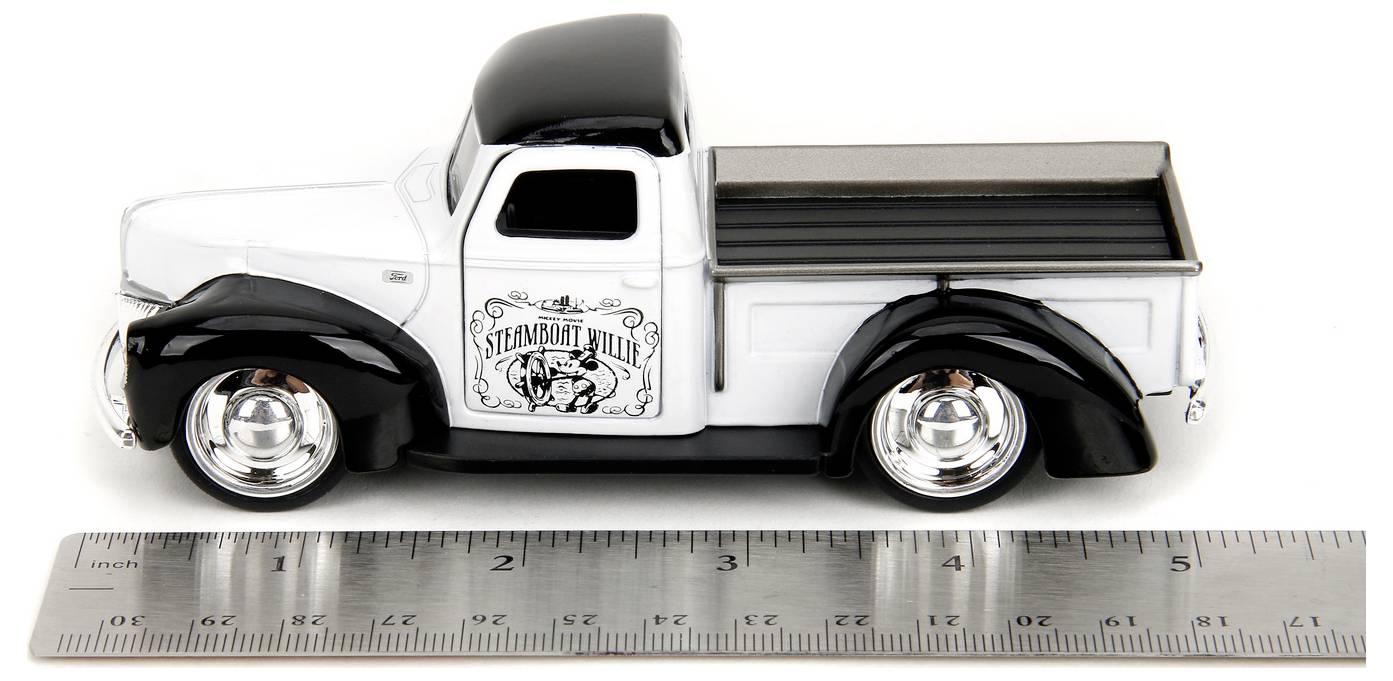 Mały modelowy samochód ciężarowy z logo 'Steadmont Willy' na drzwiach, zaparkowany obok linijki, która wskazuje, że długość pojazdu wynosi około 3 cali.