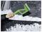 Dłoń osoby używa zielonej szczotki do usuwania śniegu z przedniej szyby samochodu, prezentując metodę konserwacji pojazdu w zimie.