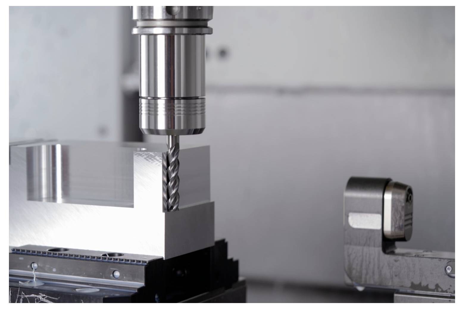 Zbliżenie na frezarkę CNC wiercącą otwory w prostokątnym bloku metalowym. Precyzyjna głowica obróbcza maszyny jest wyraźnie widoczna, podkreślając przemysłowy charakter produkcji.