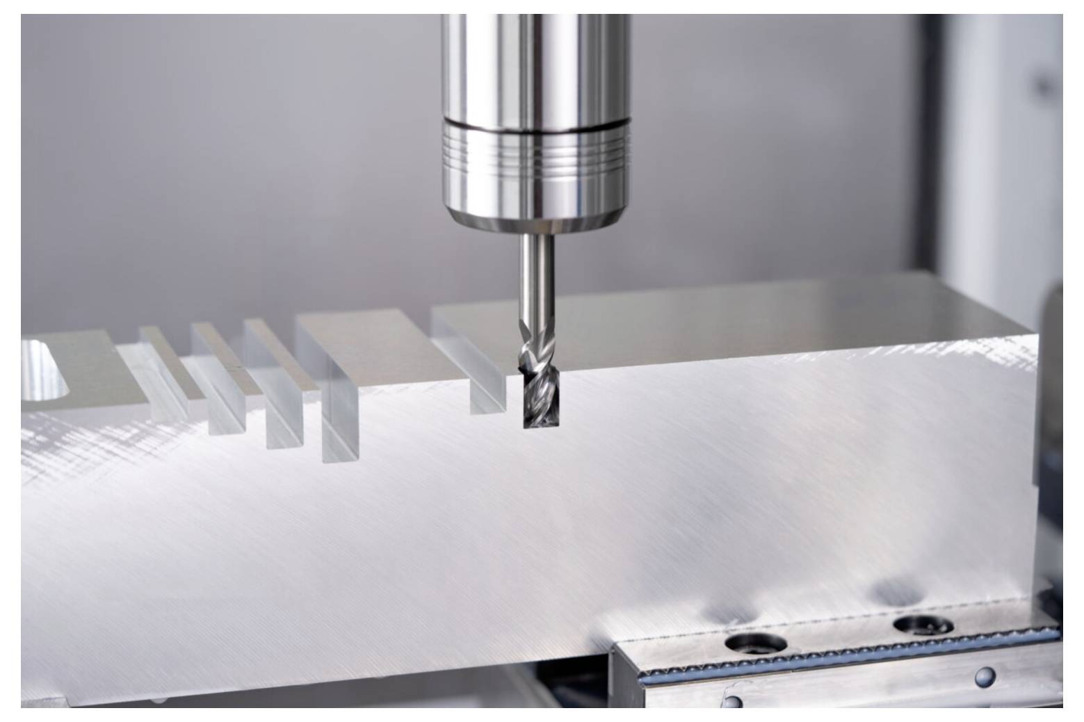 Metalowa maszyna frezująca wycina precyzyjne rowki w prostokątnym elemencie metalowym, prezentując przemysłowe procesy produkcyjne.