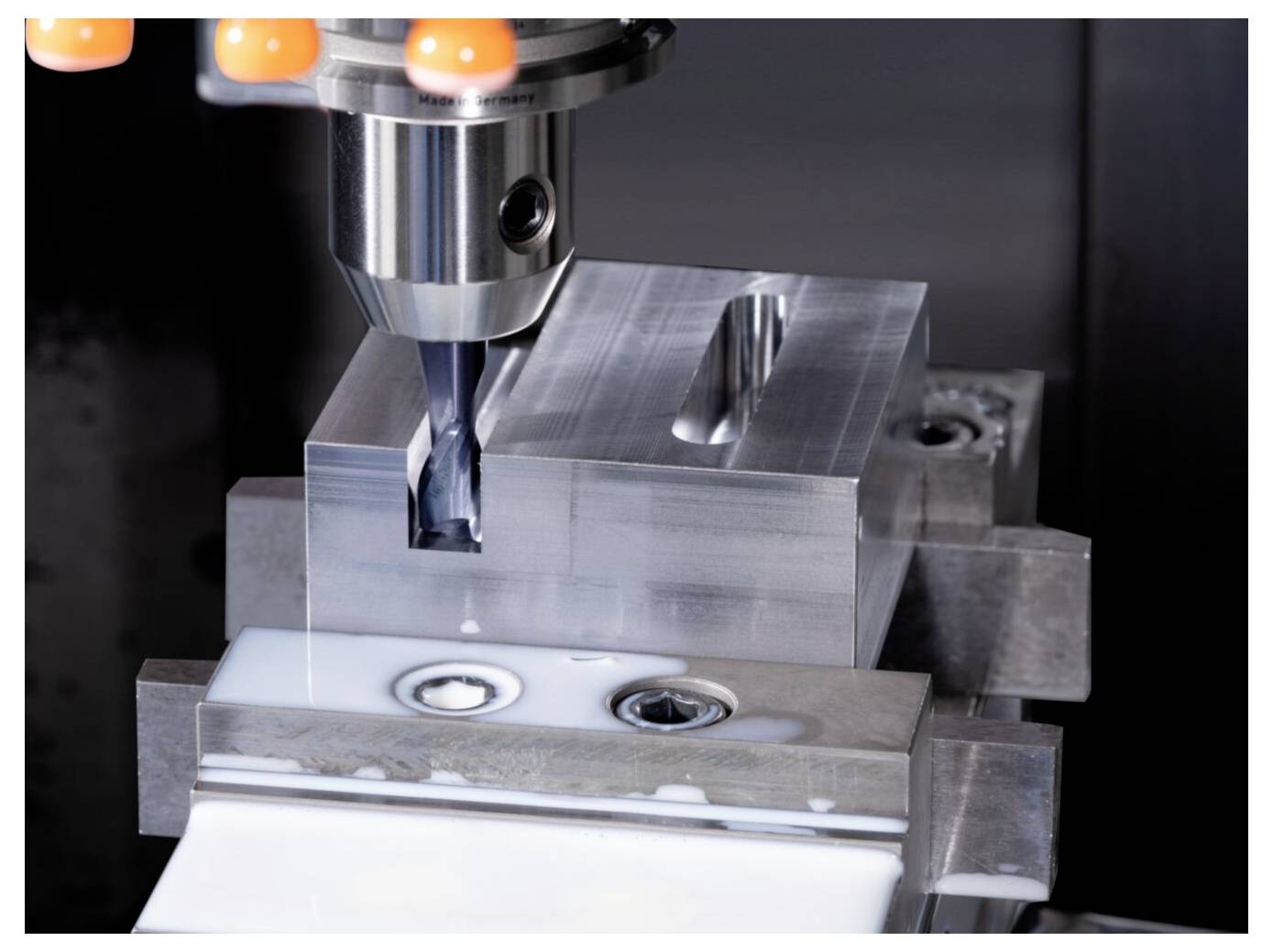 Pionowe frezowanie CNC realizowane jest na prostokątnym bloku metalowym, gdzie obrabiarka wytwarza gładkie krawędzie na stole roboczym przy zastosowaniu płynu chłodzącego.