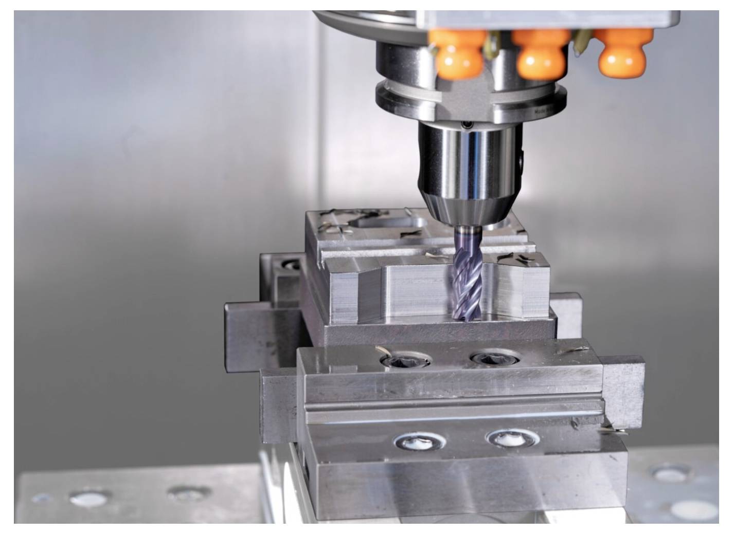 Maszyna CNC do frezowania obrabiająca blok metalowy, z szarymi elementami mechanicznymi i przemysłowym tłem, prezentująca precyzyjną produkcję.