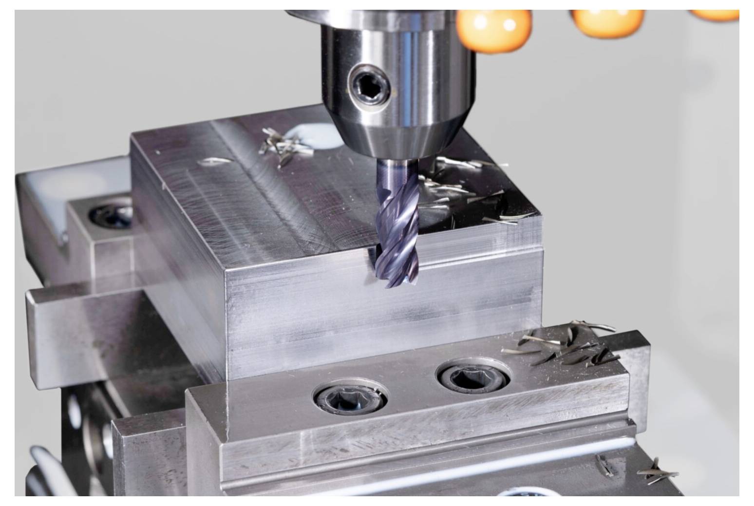 Metalowa maszyna CNC frezująca prostokątną bryłę, tworząca gładkie powierzchnie. Wokół bryły widoczne są wióry metalowe.