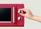 Ręka reguluje pokrętło zegara na czerwonym mikrofalówce, z widocznym w pobliżu ustawieniem mocy.
