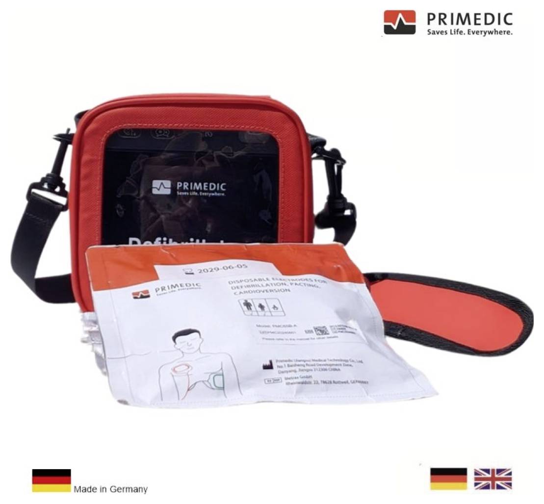 Czerwona torba defibrylator marki PRIMEDIC zawierająca sprzęt medyczny. U dołu widoczne napisy "Made in Germany" i flaga brytyjska.