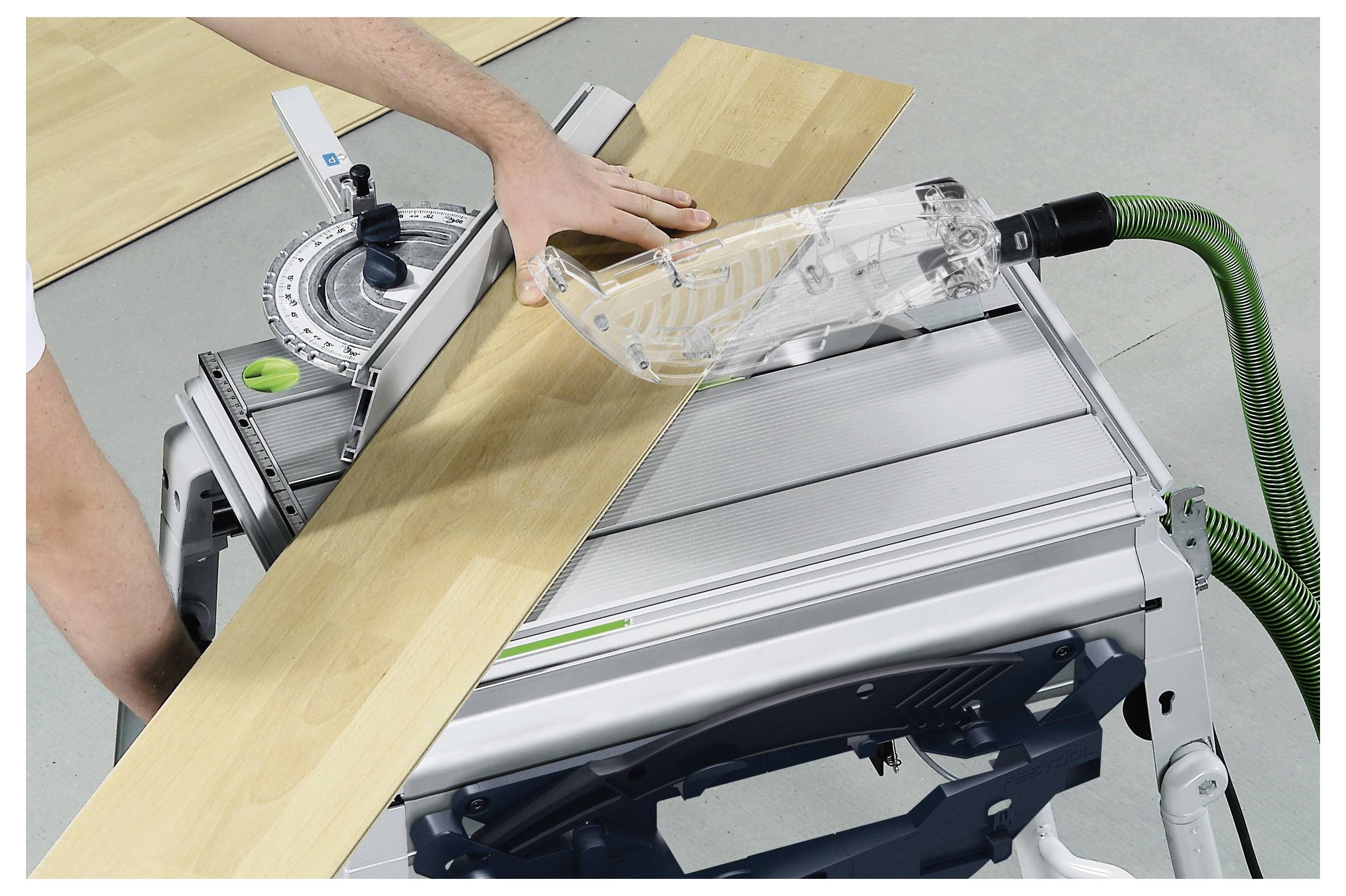 Osoba prowadzi drewnianą deskę przez piłę stołową ze sprzętem zabezpieczającym ostrze, zapewniając precyzyjne cięcie. Widoczny jest sprzęt ochronny.